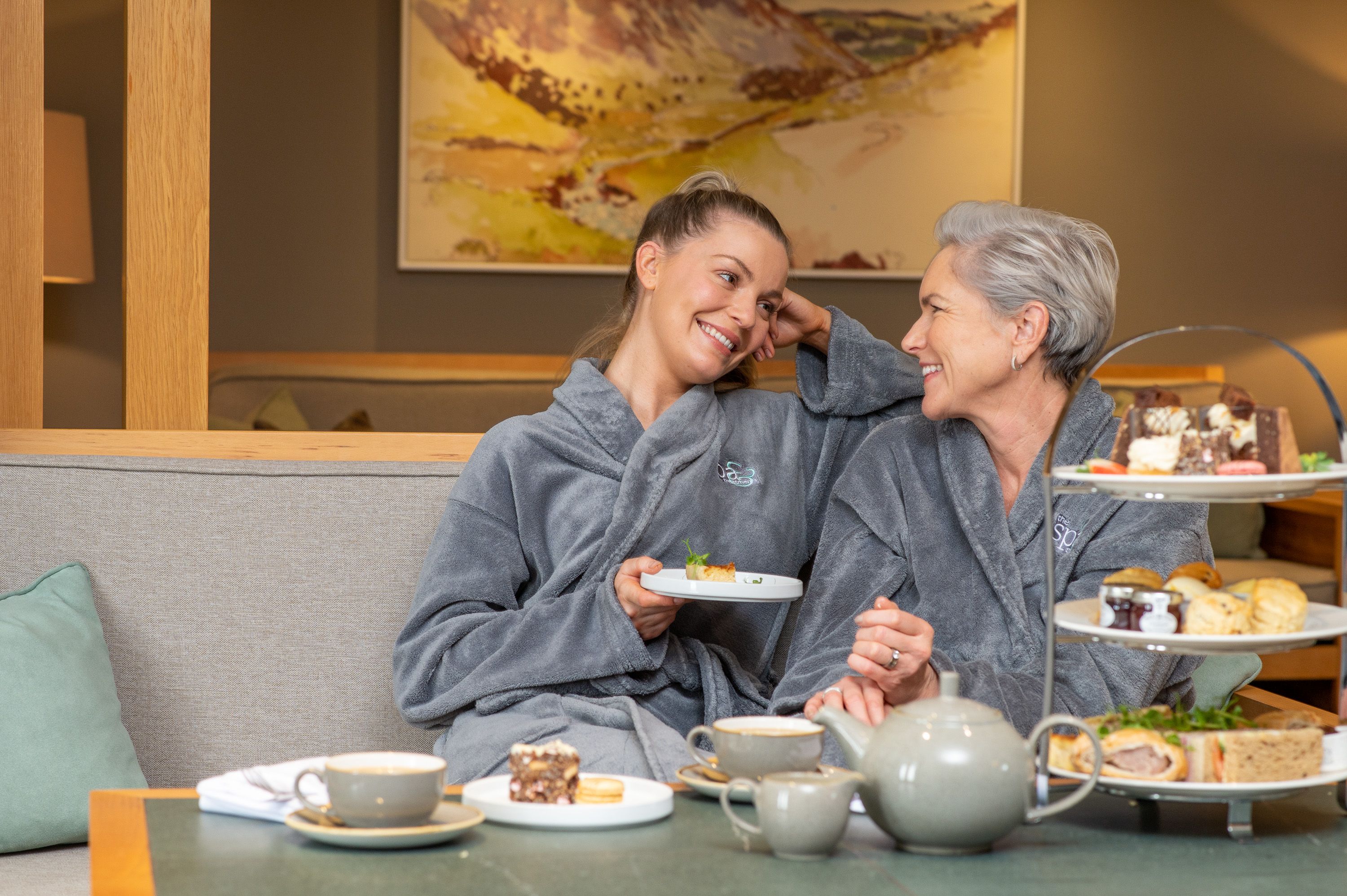 two women in bathrobes having tea and snacks