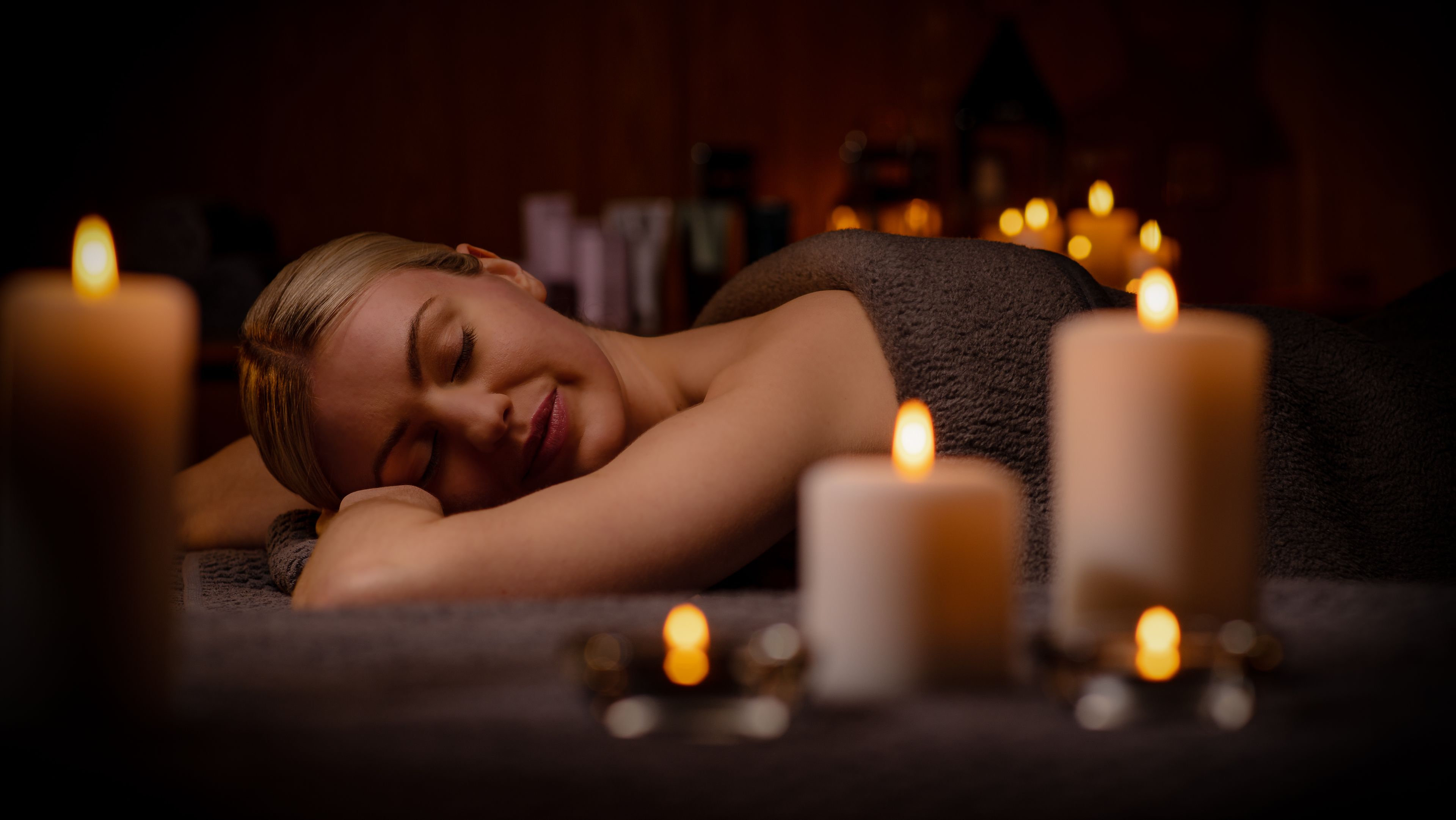 a person in a towel lying down on a spa table with her eyes closed and candles surrounding her