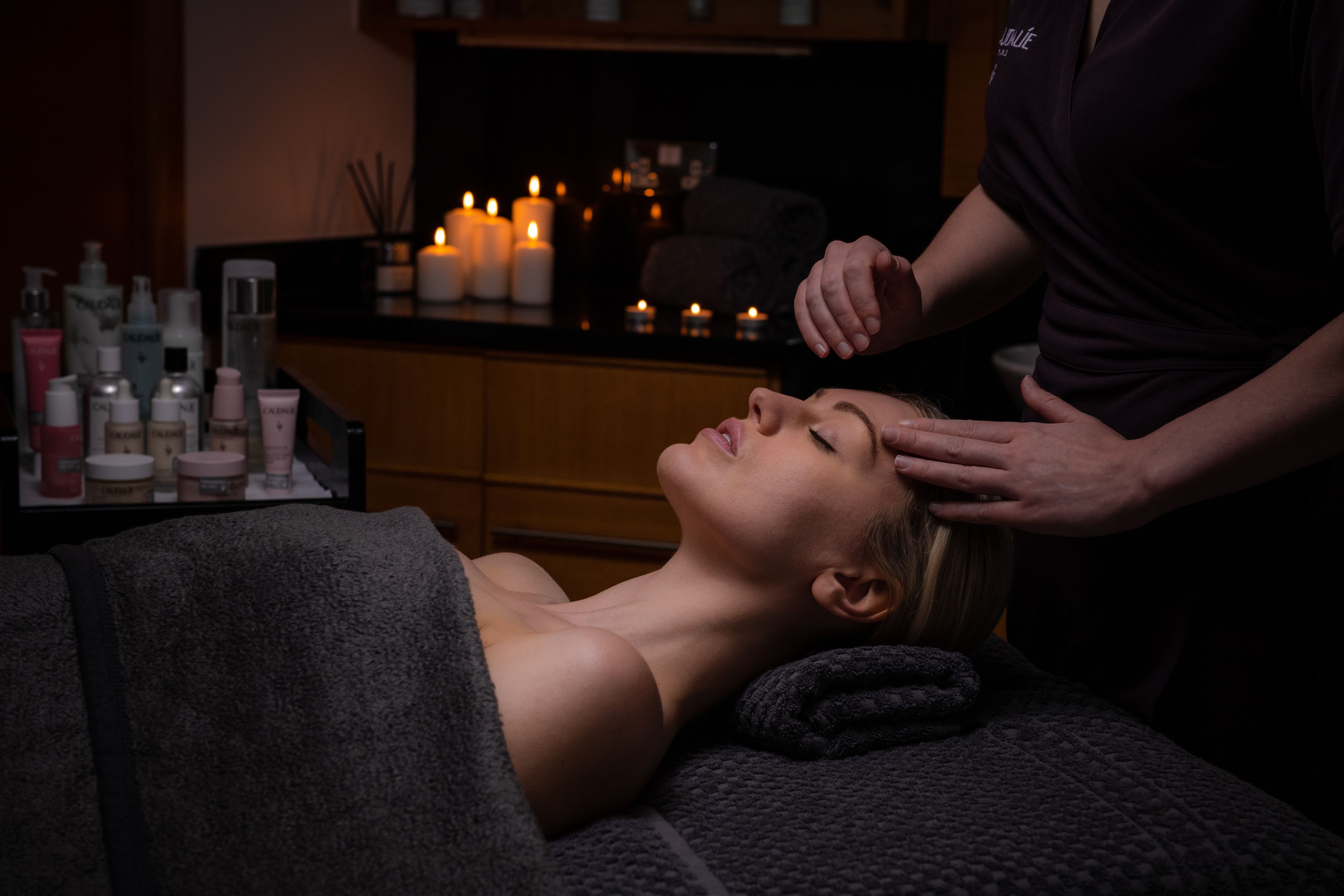 person receiving a head massage on a spa table with candles in the background