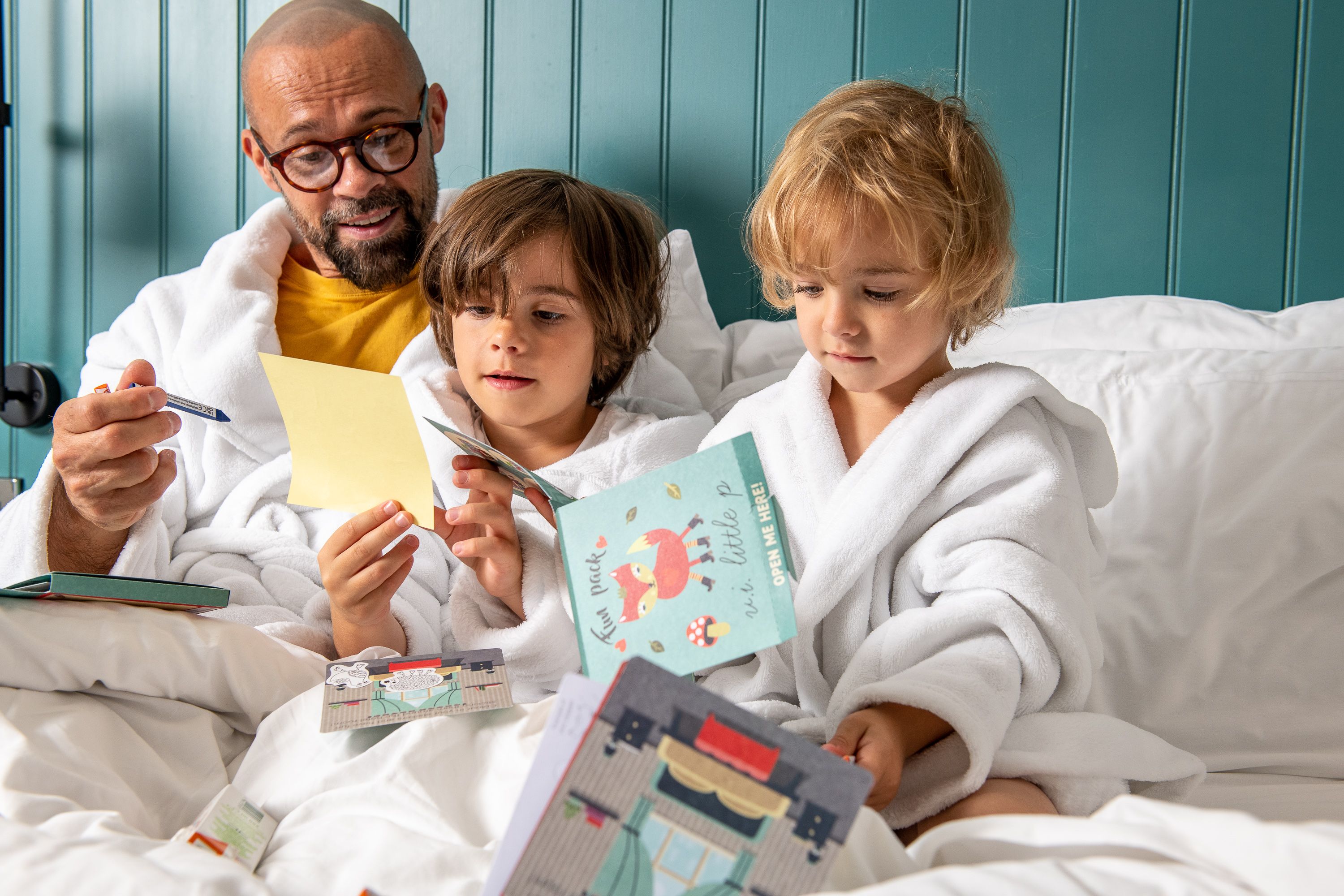 two children and a person in bathrobes completing activity booklets in bed