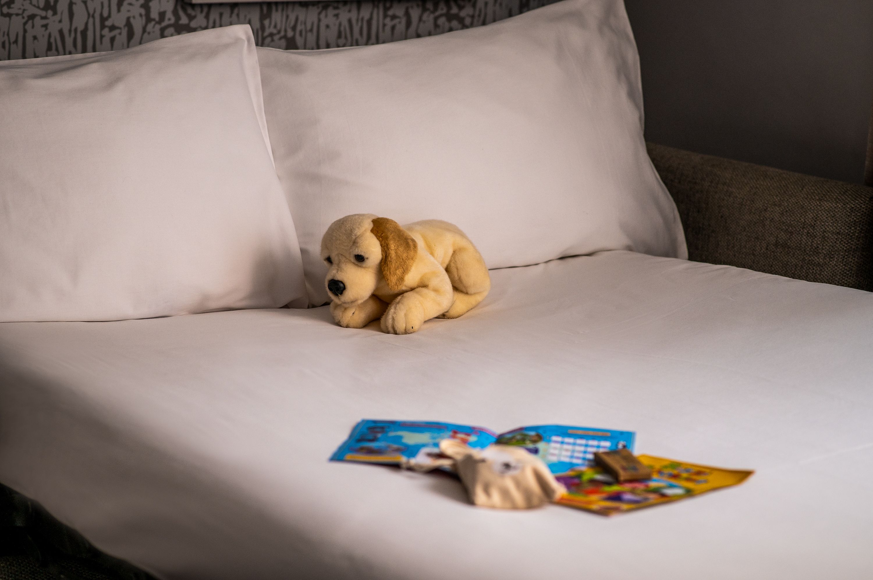 bed with white sheets, a stuffed dog, and children's books