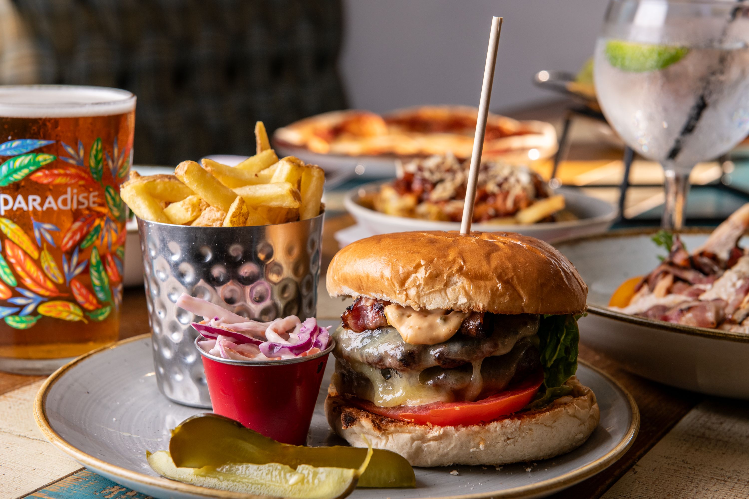 burger, chips, coleslaw and pickles on a plate with a pint of beer