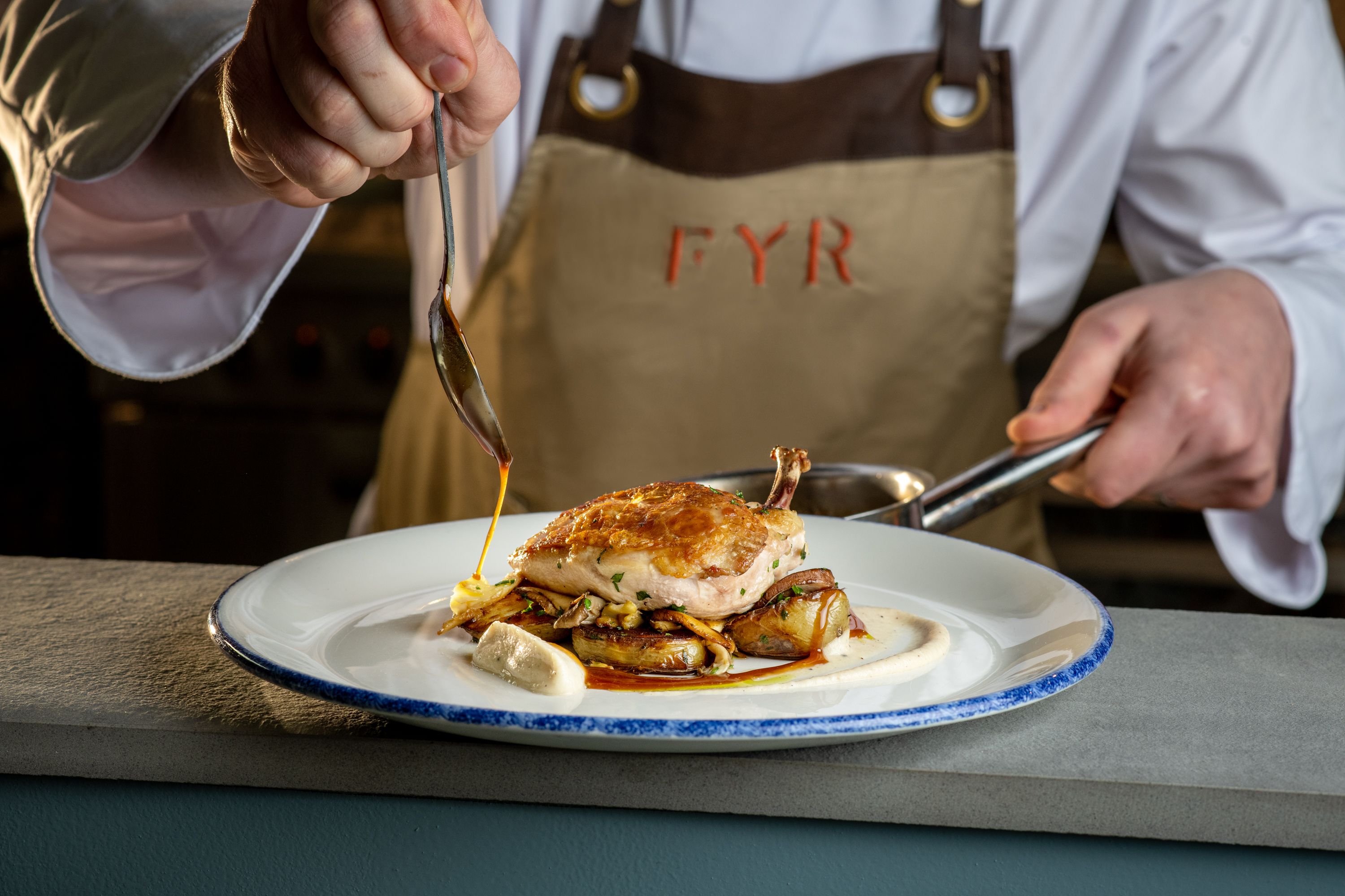 chef pouring sauce on a chicken dish