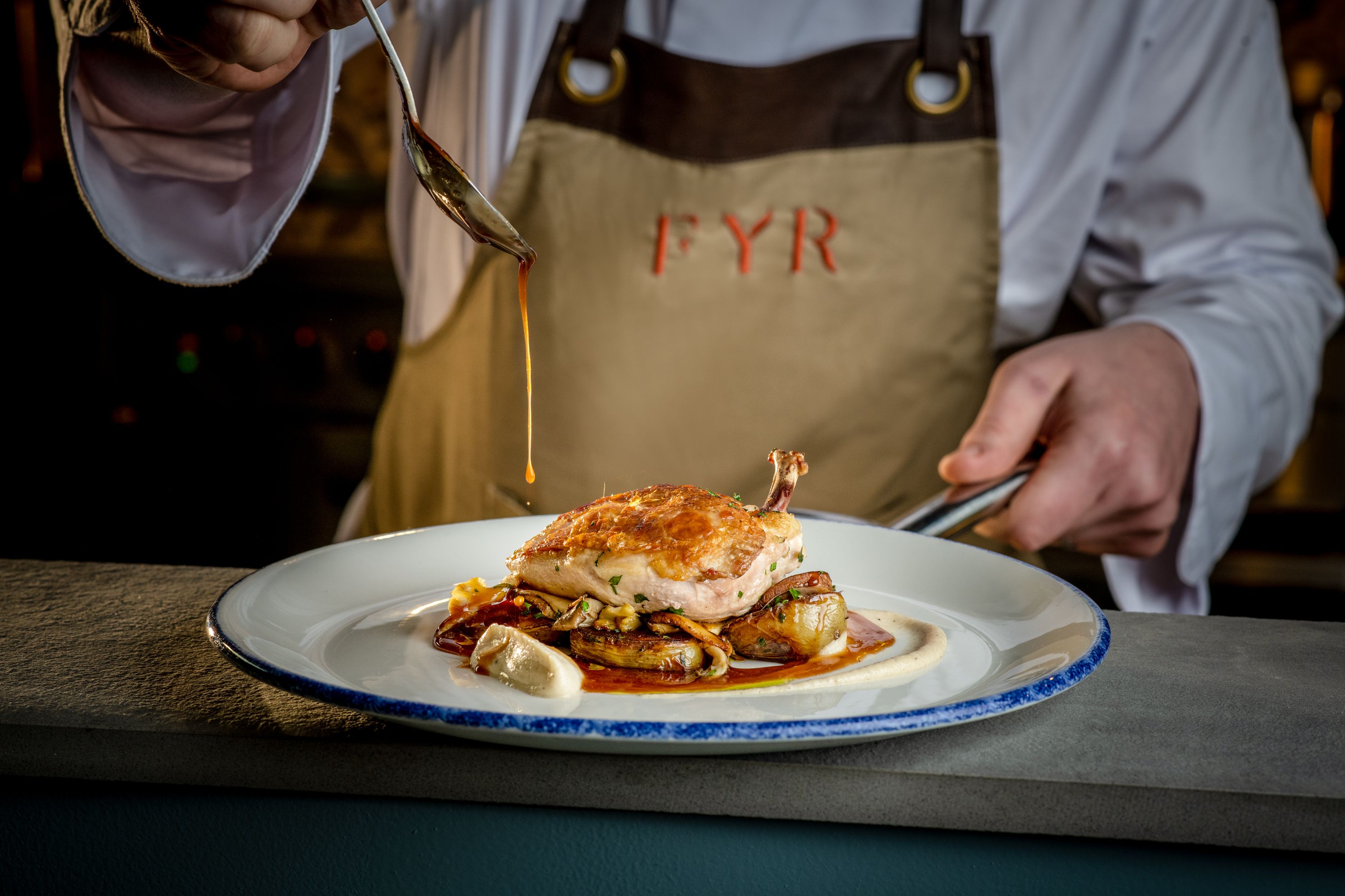 chef pouring sauce on a chicken dish